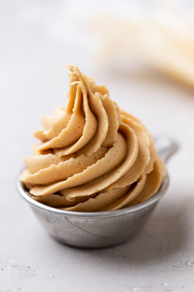 A small metal measuring cup filled with peanut butter frosting.