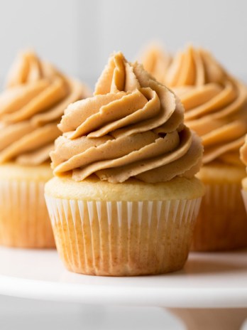 A marble cake stand holding several vanilla cupcakes topped with peanut butter frosting.