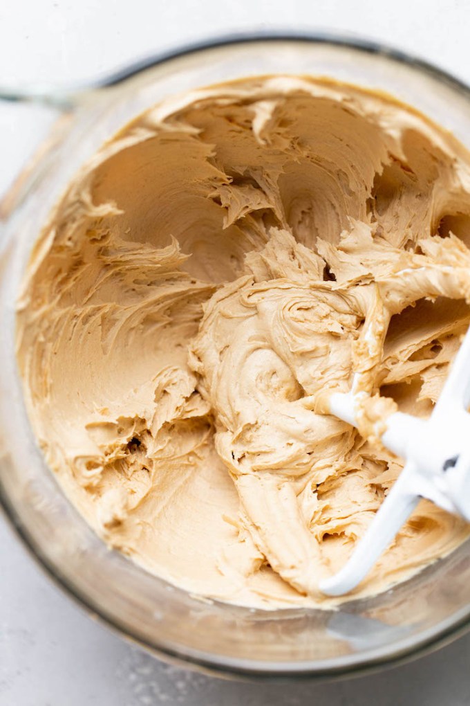 A glass mixing bowl holding finished peanut butter frosting.