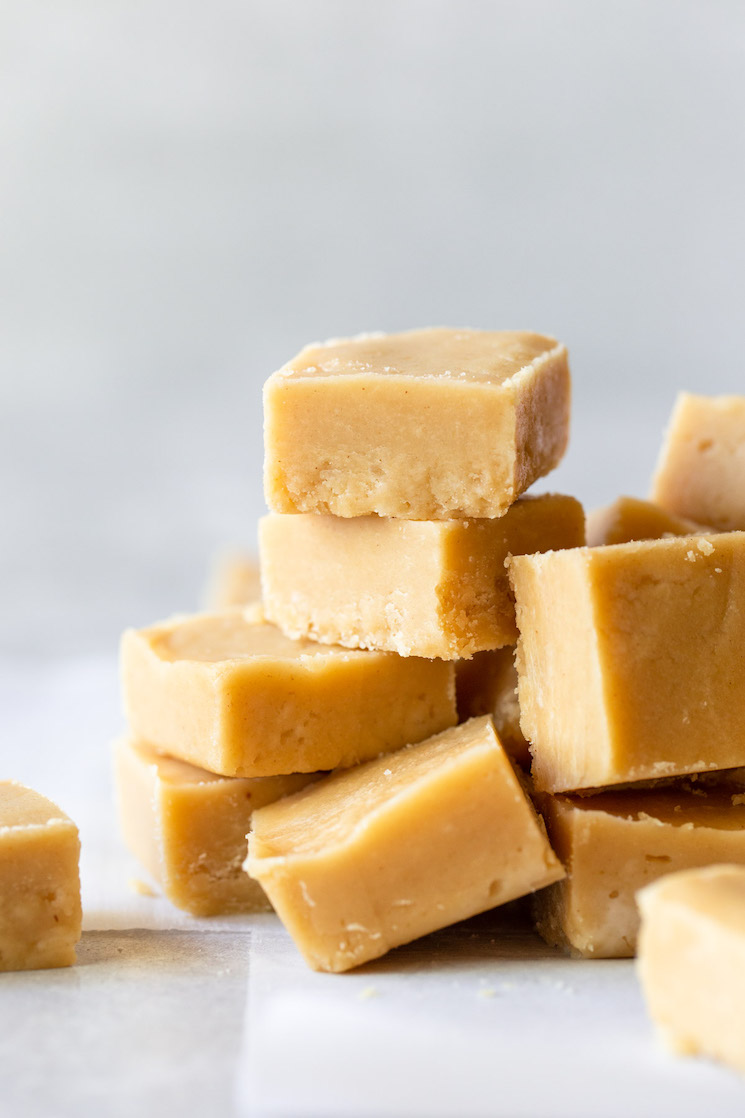 Pieces of peanut butter fudge stacked on a gray surface lined with parchment paper.
