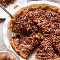 A pecan pie in a white baking dish that has been sliced.