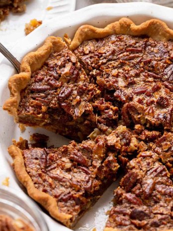 A pecan pie in a white baking dish that has been sliced.