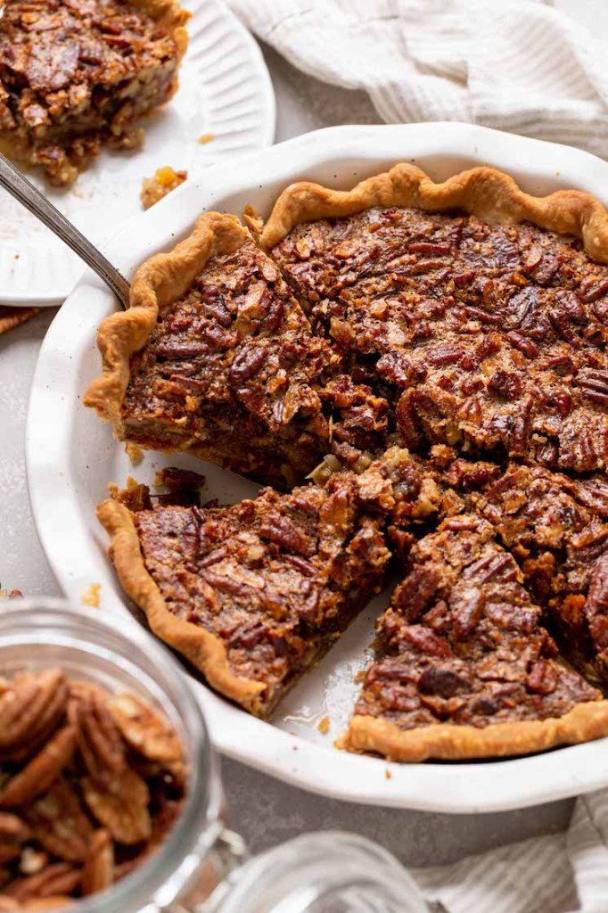 A pecan pie in a white dish that has been sliced and one slice is being removed.