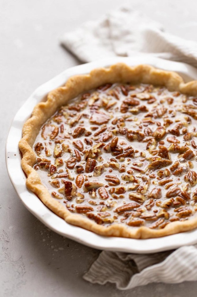 A pecan pie in a white baking dish ready to be put into the oven.
