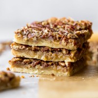 A stack of three pecan pie bars on brown parchment paper.