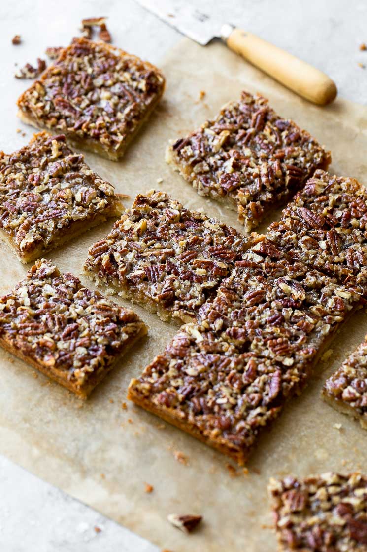 Finished pecan pie bars spread onto parchment paper with a knife in the background.