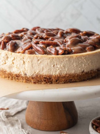 A pecan pie cheesecake sitting on top of a marble cake stand.
