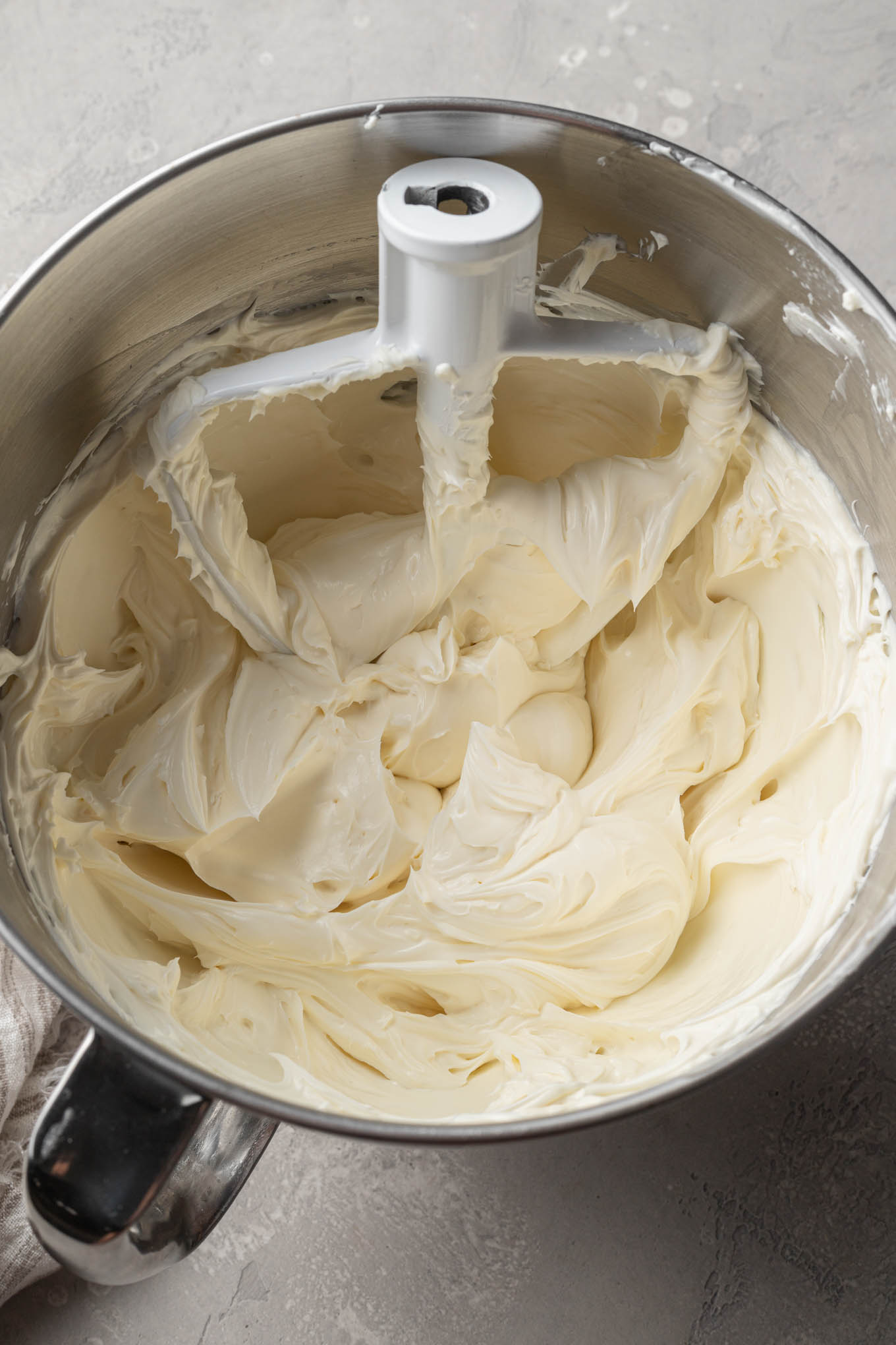 An overhead view of beaten cream cheese and sour cream in the bowl of a stand mixer, with a paddle attachment. 