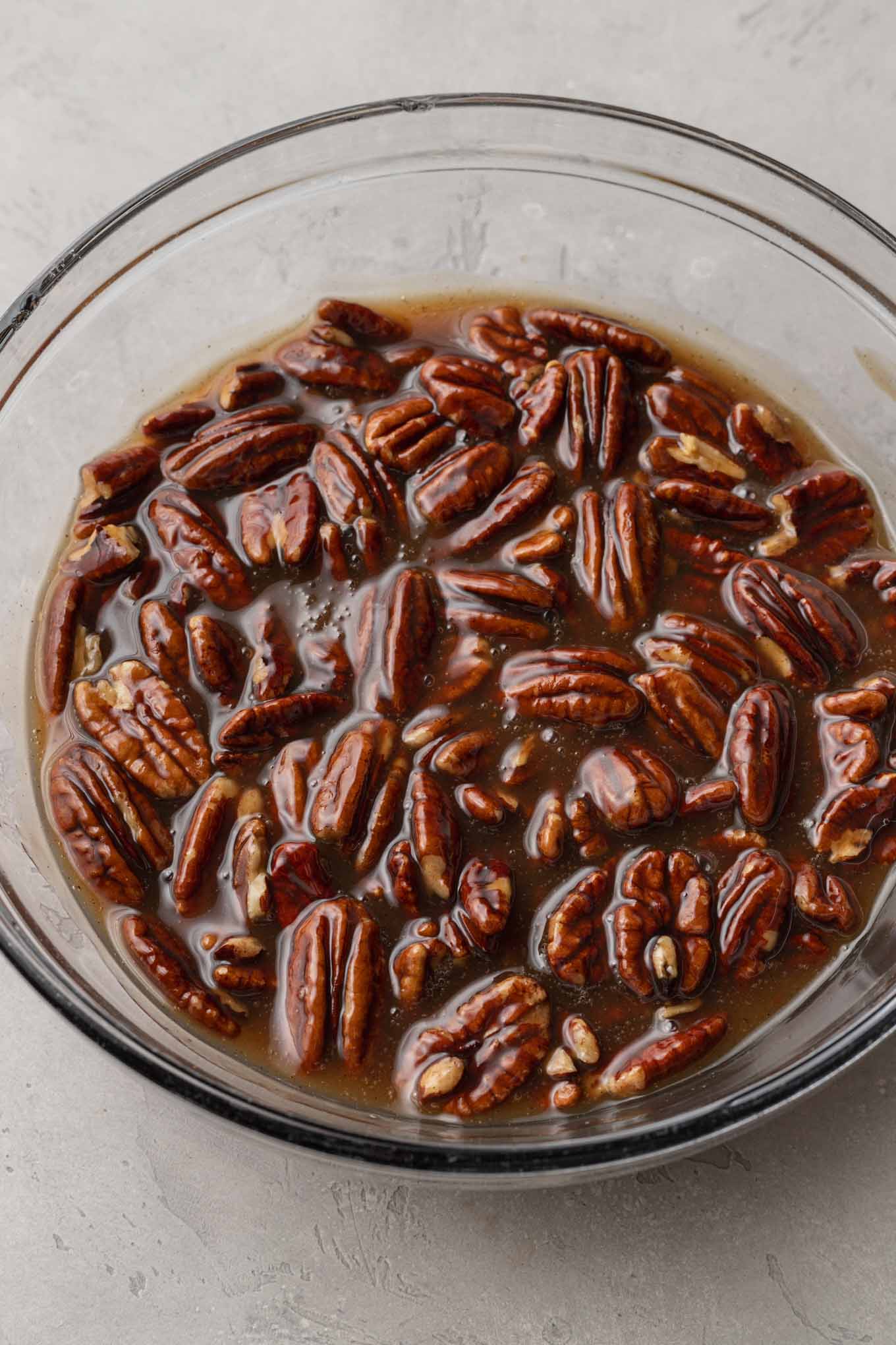An overhead view of pecan topping for a cheesecake, in a glass mixing bowl. 
