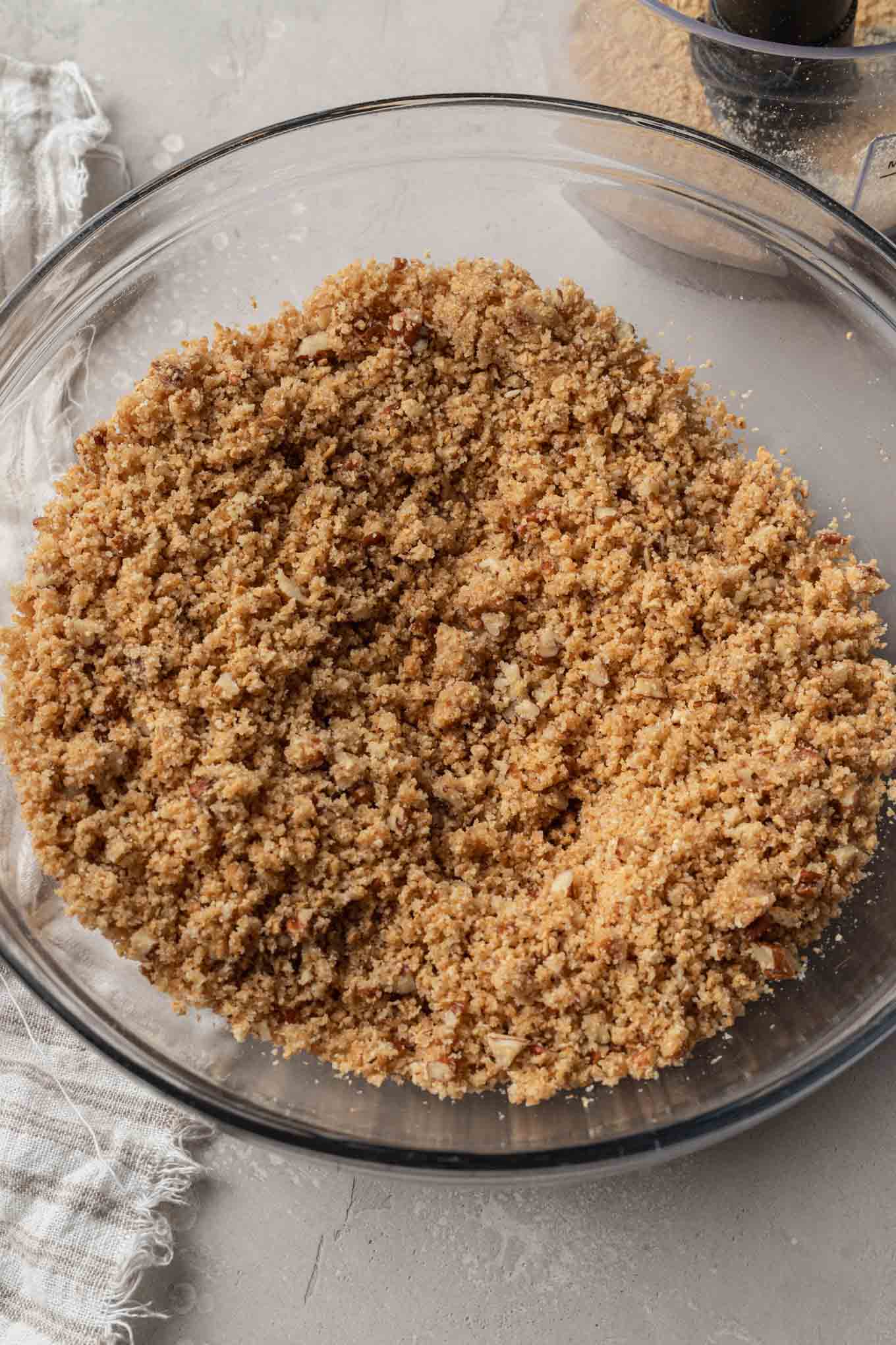 An overhead view of a graham cracker crust mixture in a glass mixing bowl. 