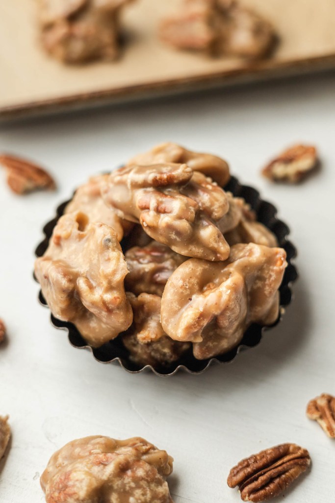 Several southern pecan pralines in a mini tart pan. Pecan halves are scattered around it. 