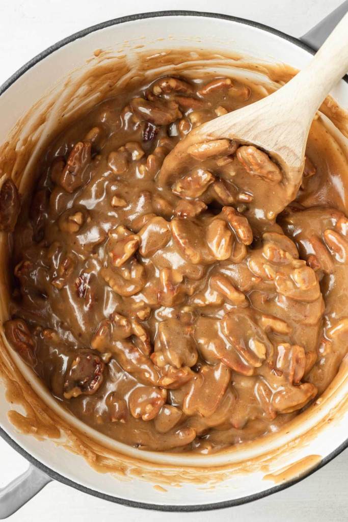 An overhead view of a pot of pecan praline mixture. A wooden spoon rests in the pot. 