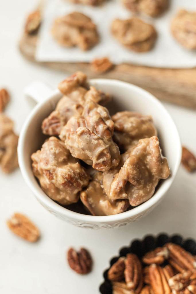 A small white dish filled with pralines. Pecan halves and additional pralines surround the dish. 