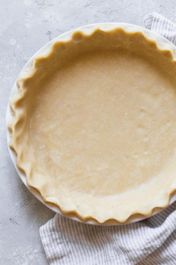 A finished pie crust in a white pie dish on top of a rustic gray surface.