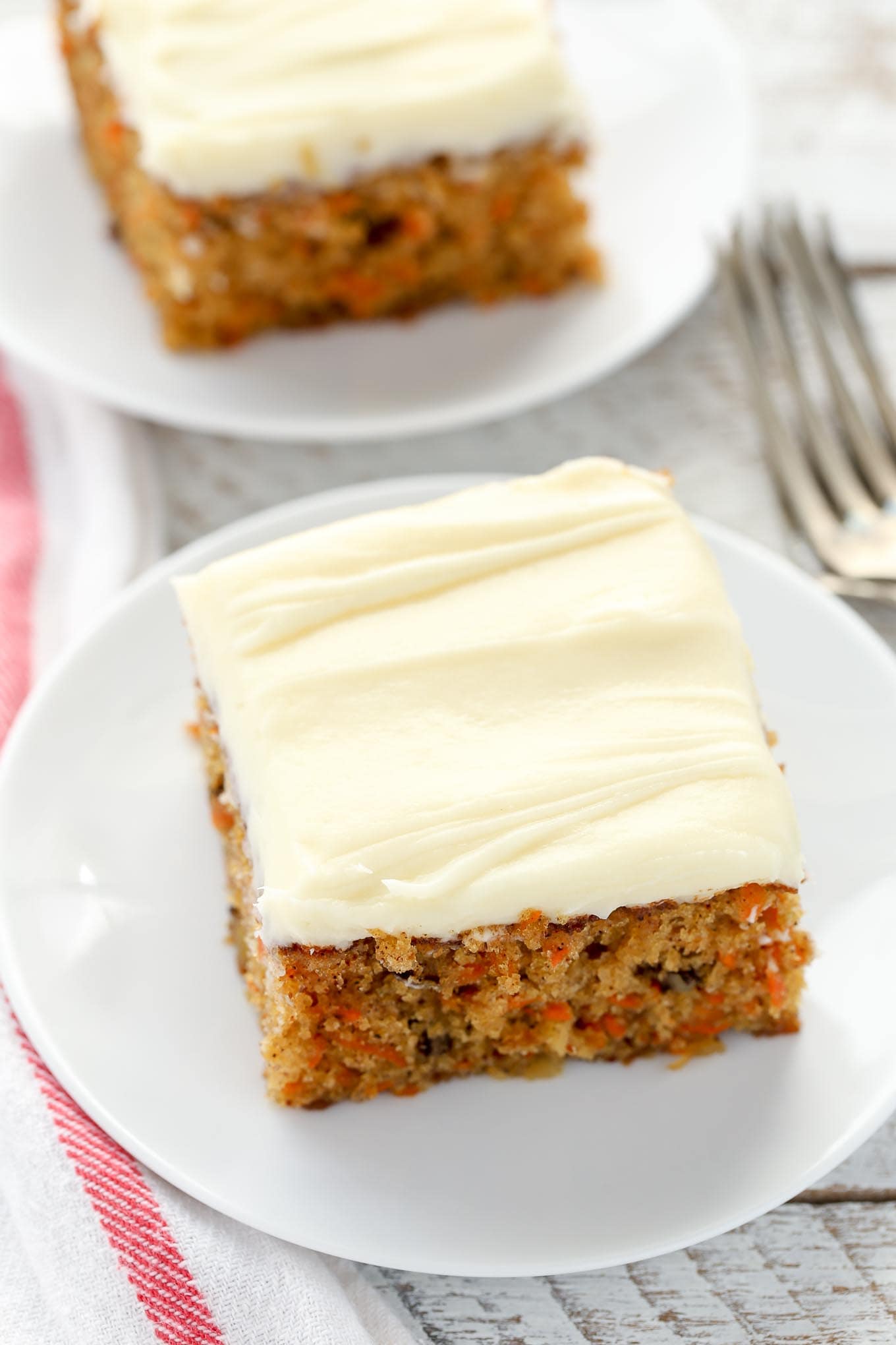 Two slices of carrot cake with pineapple on white plates. 