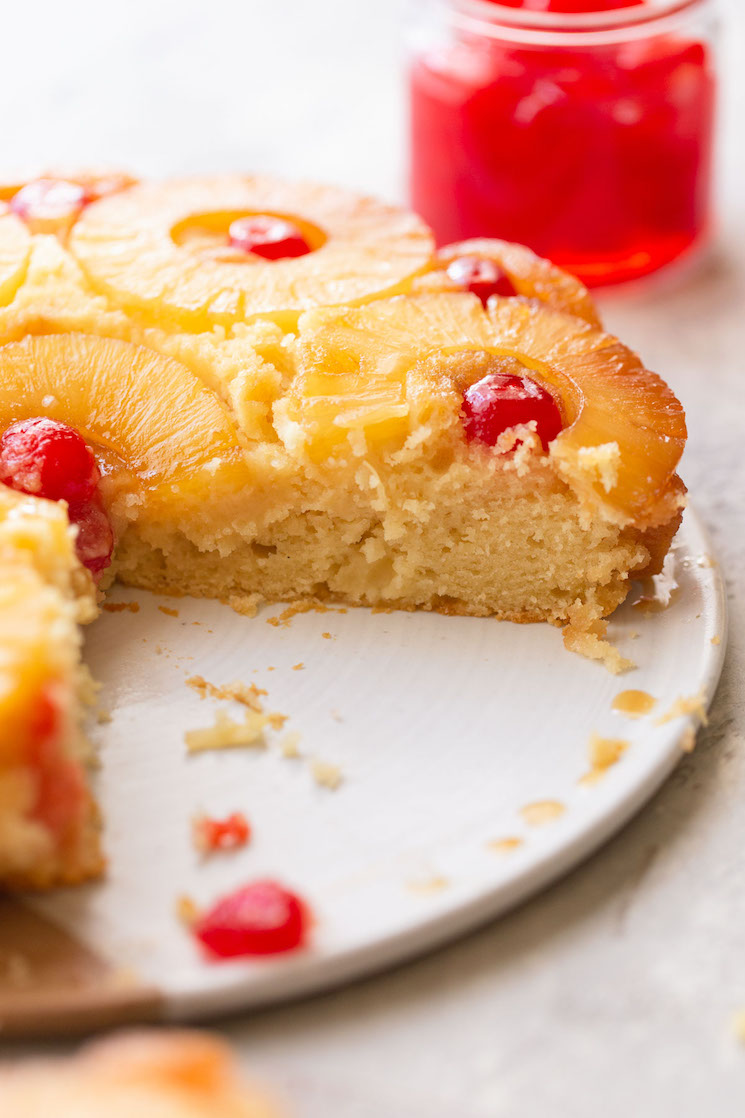 A pineapple upside down cake on a plate with one slice taken out to show the texture of the cake.