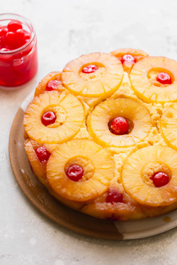 A finished pineapple upside down cake resting on a plate with a jar of cherries in the background.