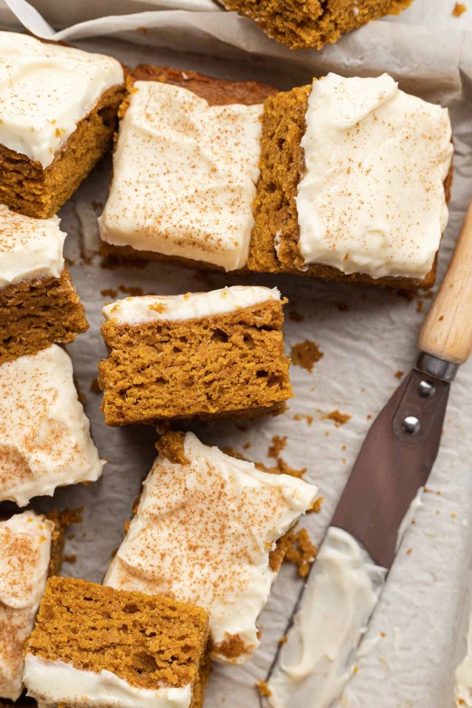 Sliced pumpkin bars with cream cheese frosting on parchment paper. Some bars are turned on their sides.