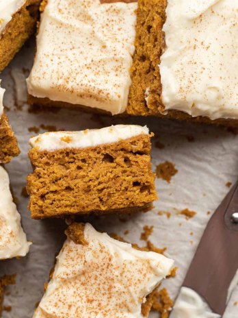 Several slices of pumpkin bars on a piece of parchment paper. One slice is turned on its side to show the texture.