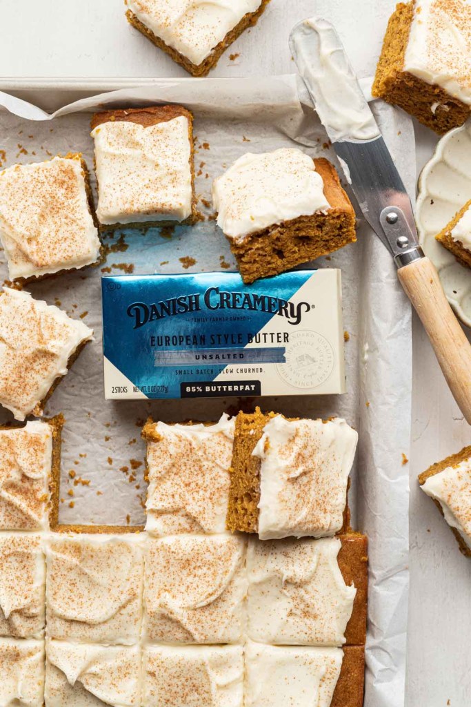 Sliced pumpkin bars with cream cheese frosting in a baking pan, with a package of Danish Creamery butter in the middle. 