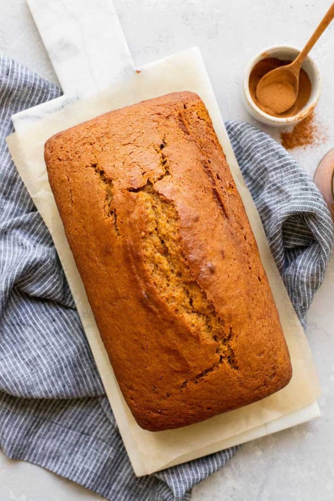 A loaf of pumpkin bread cooling on a marble serving tray with cinnamon in a bowl in the background.