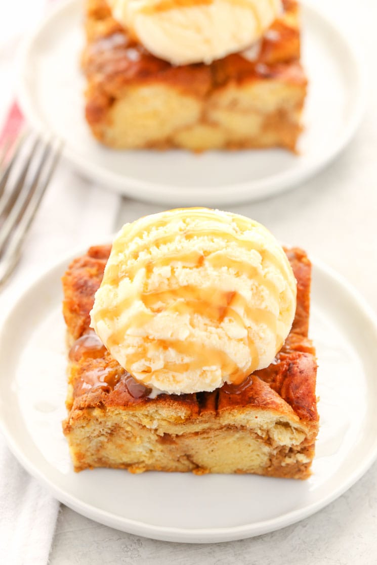 Two slices of pumpkin bread pudding topped with ice cream and caramel sauce on white plates. 