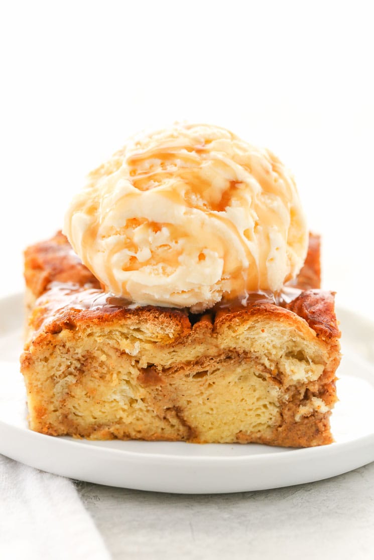 Slice of pumpkin bread pudding topped with ice cream on a white plate. 