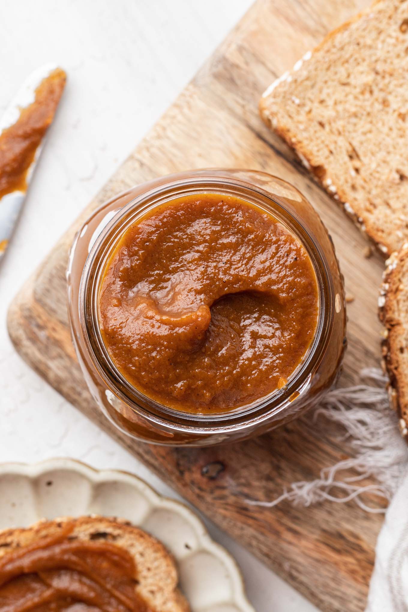 An overhead view of a jar of pumpkin butter on a wood board with bread slices. 