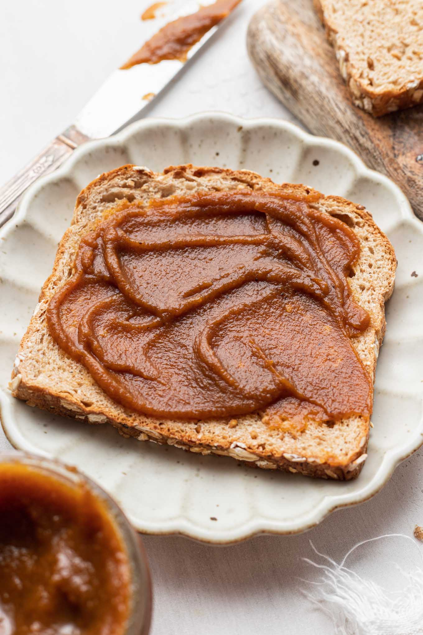 A slice of toast slathered with pumpkin butter on a white plate. 