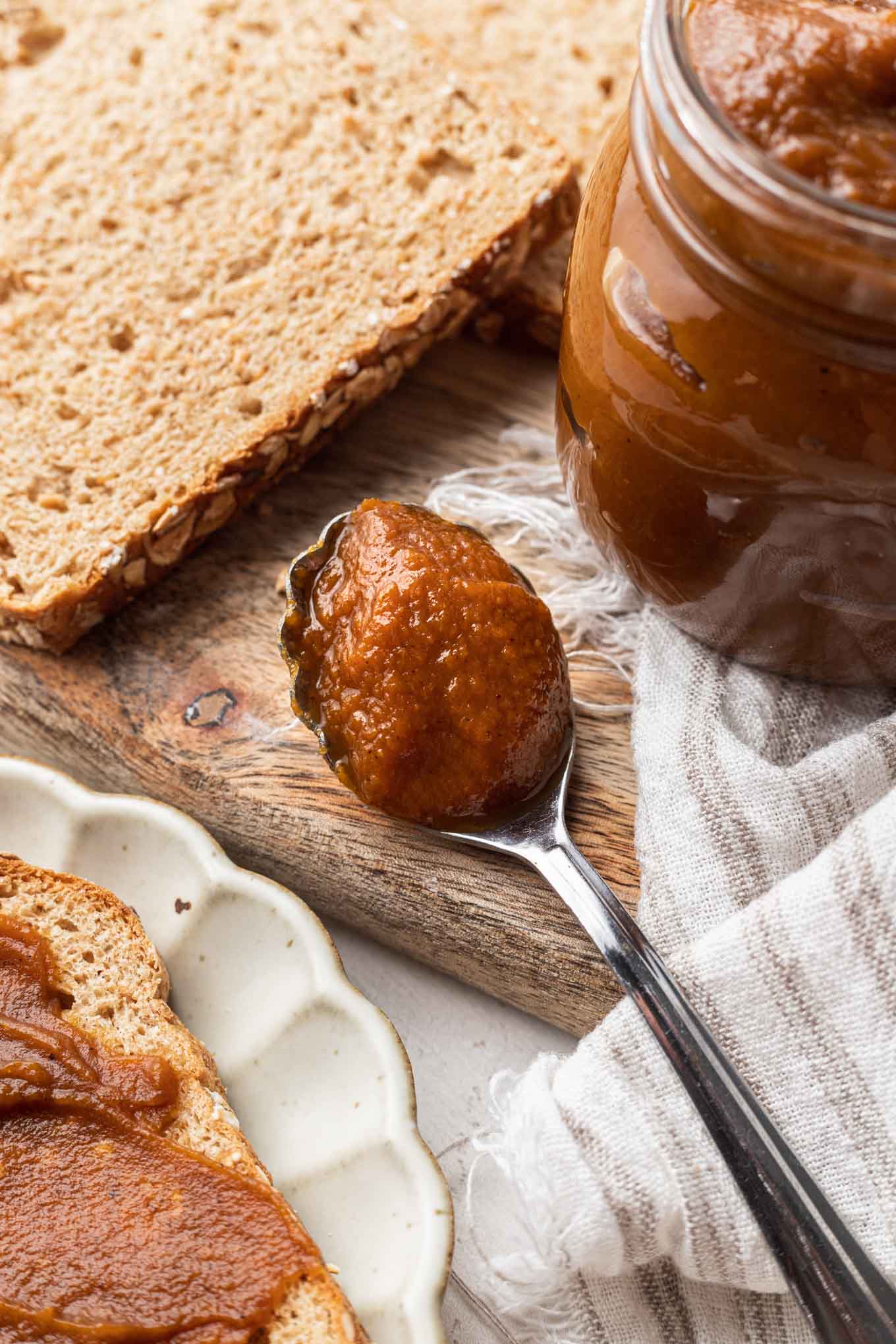 A spoonful of pumpkin butter next to a jar and bread slices. 