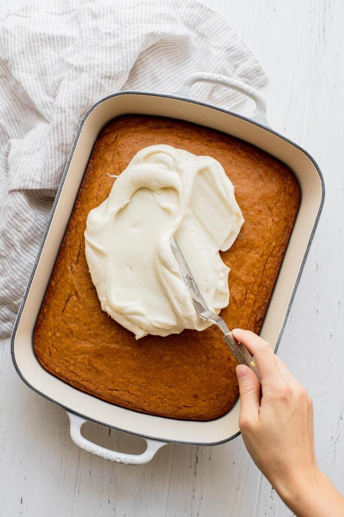 Cream cheese frosting being spread out on top of a pumpkin cake.