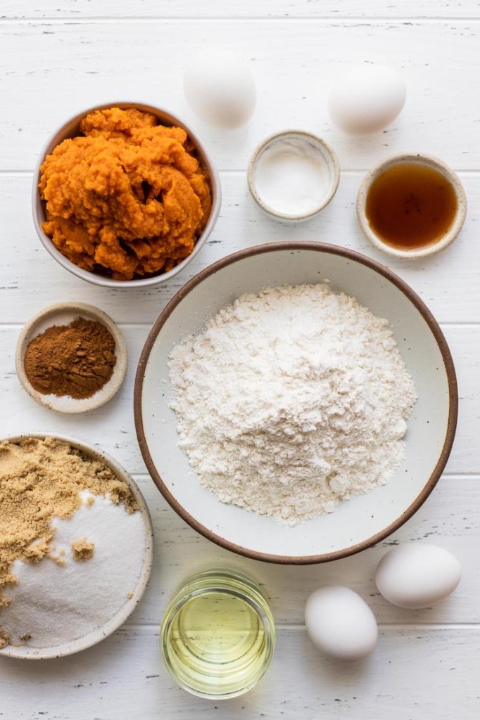 The ingredients needed to make pumpkin cake on a rustic white wood surface.