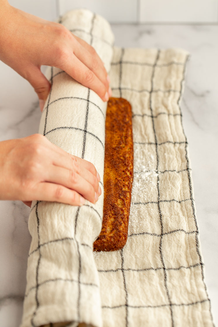 The pumpkin cake being rolled up into a towel dusted with powdered sugar while it's still warm.