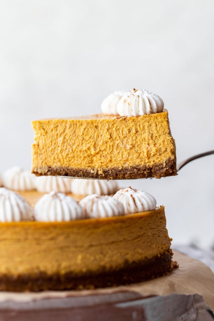 A single piece of pumpkin cheesecake being lifted away from the rest of the cheesecake showing the creamy texture.