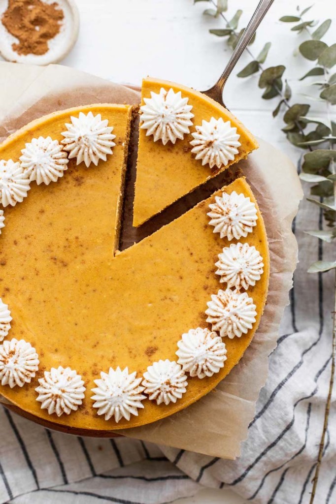 An overhead view of a whole cheesecake with one piece cut and being pulled out.