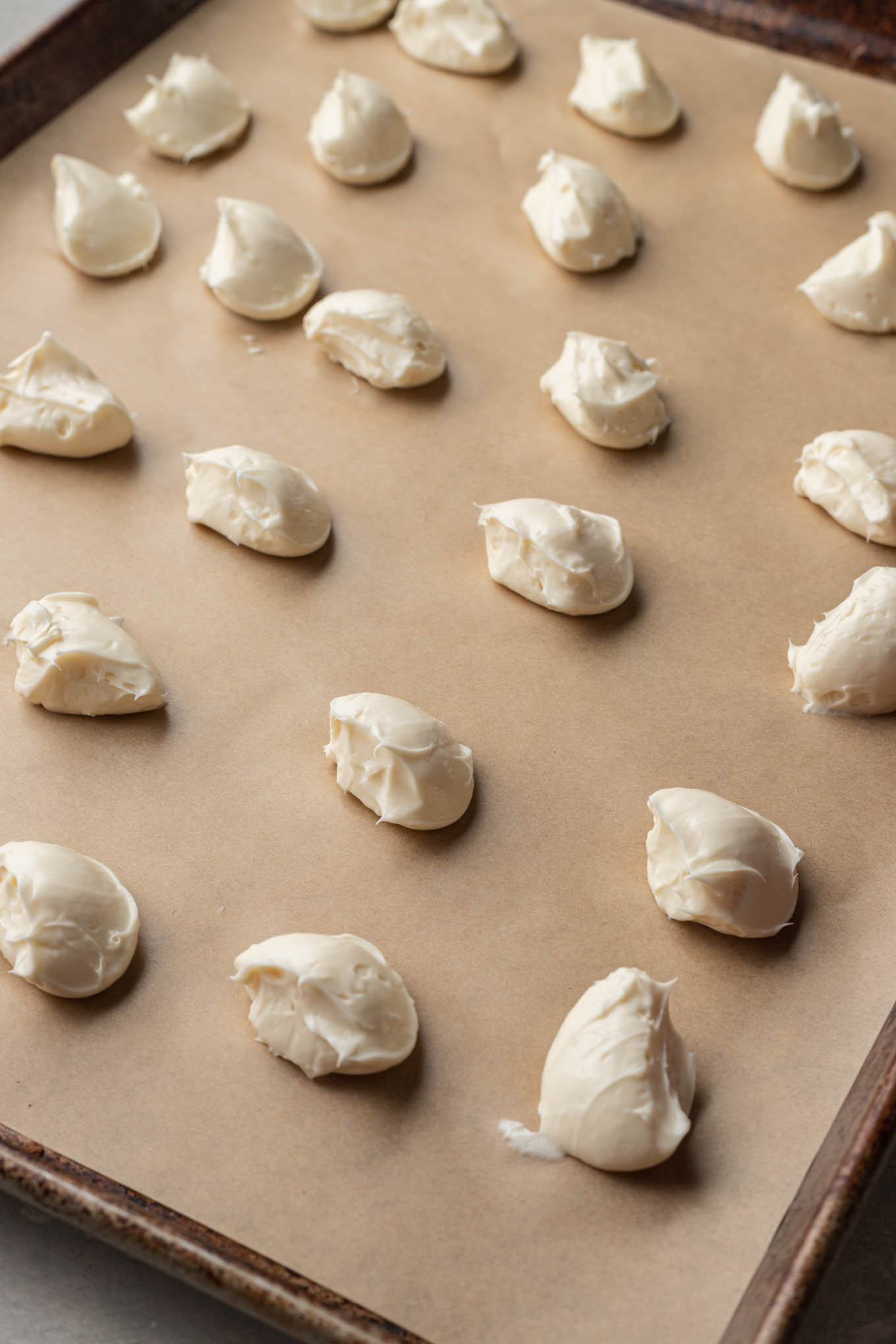 Scoops of cheesecake filling on a parchment paper-lined cookie sheet. 