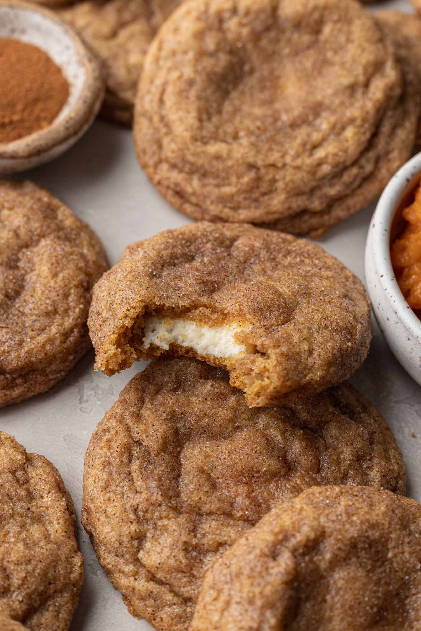 A pumpkin cheesecake cookie, bitten to show the filling, resting atop other cookies. 