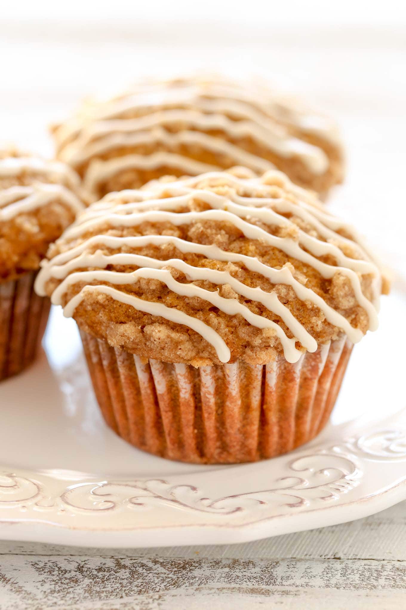 Three of the best ever pumpkin muffins topped with vanilla glaze on a white plate. 