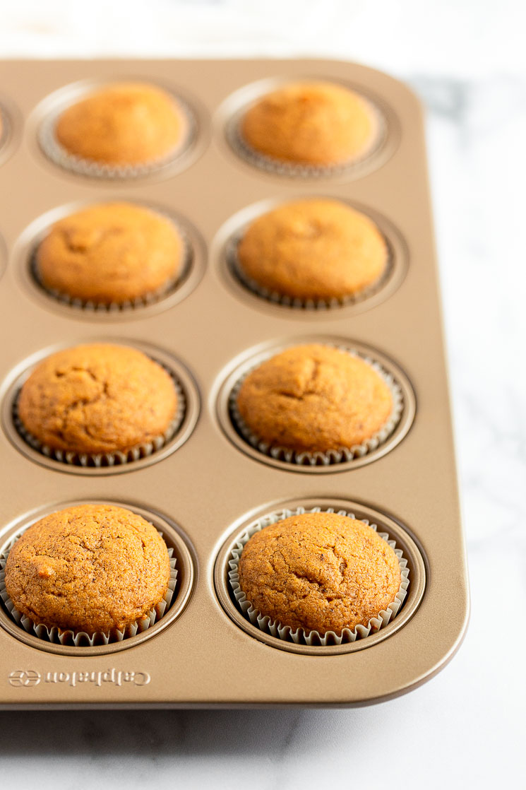 A muffin pan filled with pumpkin cupcakes fresh out of the oven.