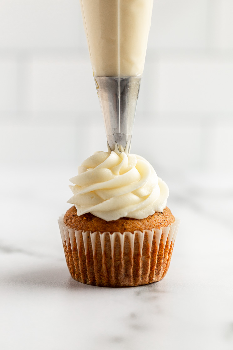 A single pumpkin cupcake being topped with cream cheese frosting using a piping bag.