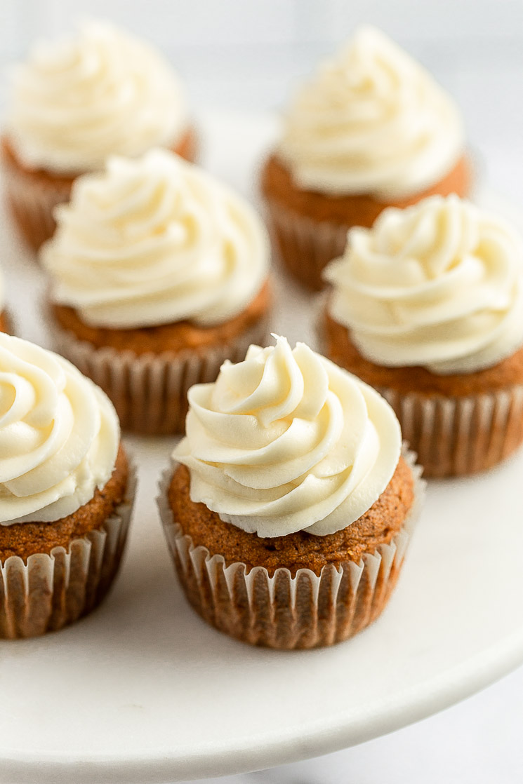 An overhead shot of a group of pumpkin cupcakes topped with cream cheese frosting.