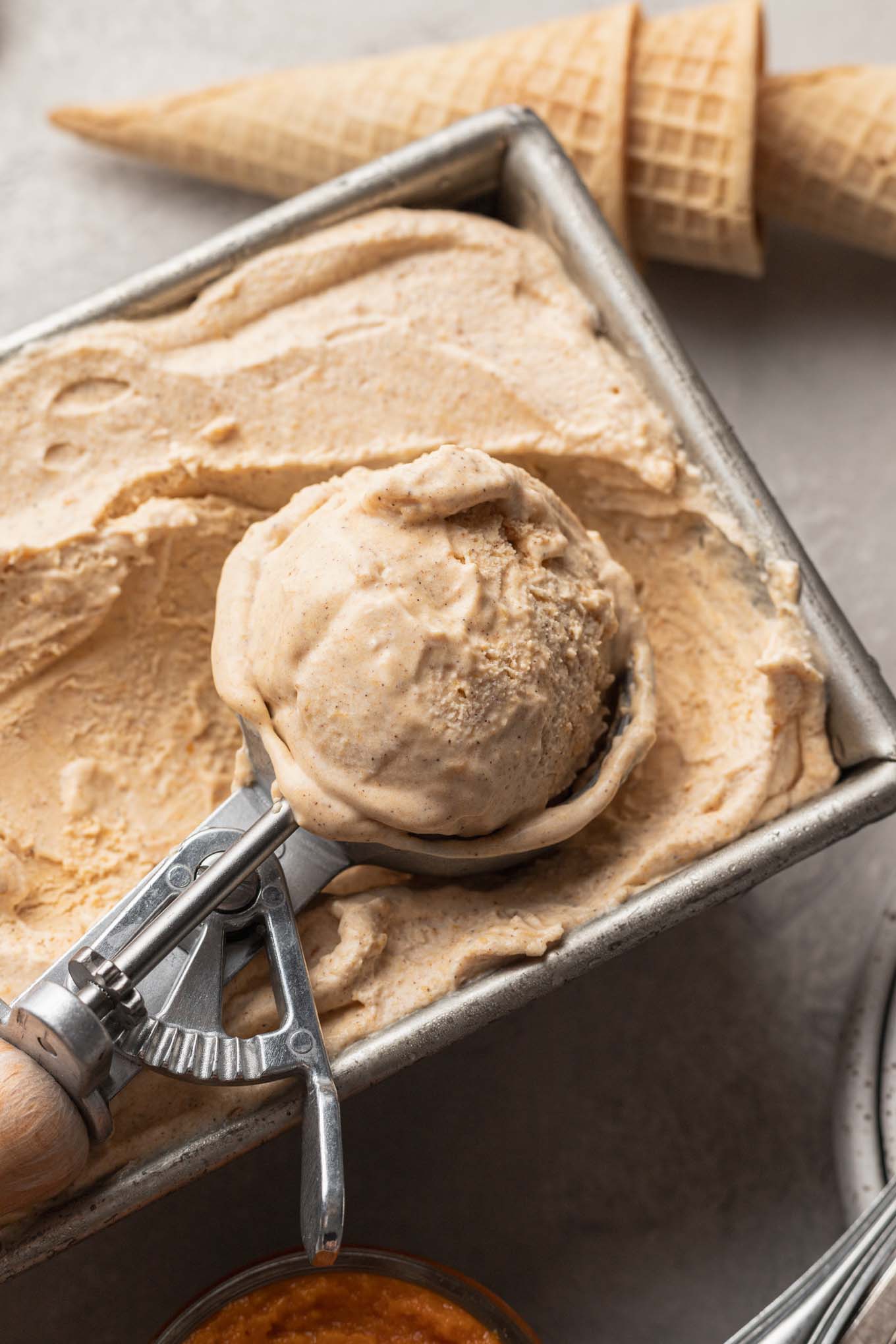 Pumpkin ice cream in a loaf pan, being scooped with an ice cream scoop. 