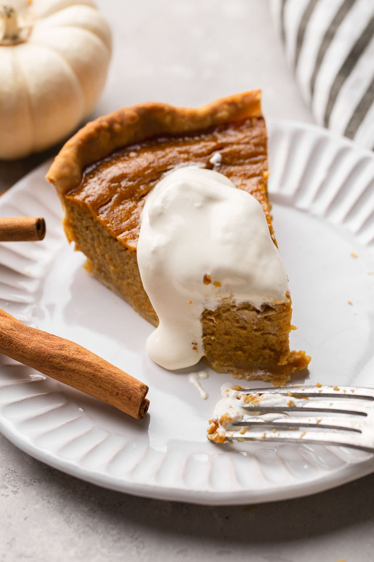 A slice of homemade pumpkin pie topped with whipped cream on a white plate. 