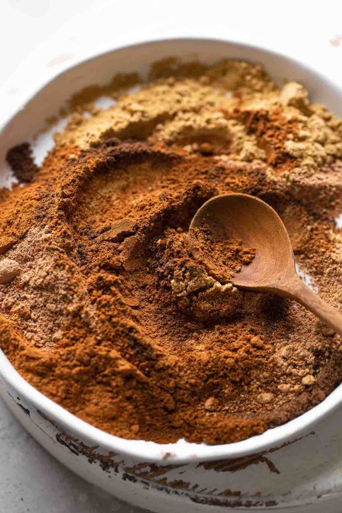 A wooden spoon mixing together the spices for pumpkin pie spice on a white dish.