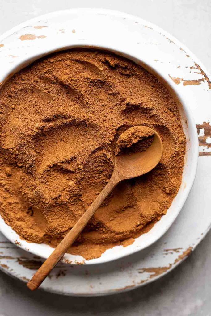Pumpkin pie spice mixed together on a white plate. A brown spoon rests on top of the spices.