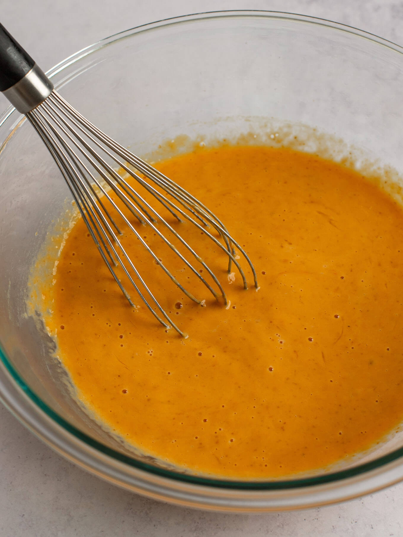 The wet ingredients for pumpkin pie whisked together in a glass mixing bowl.