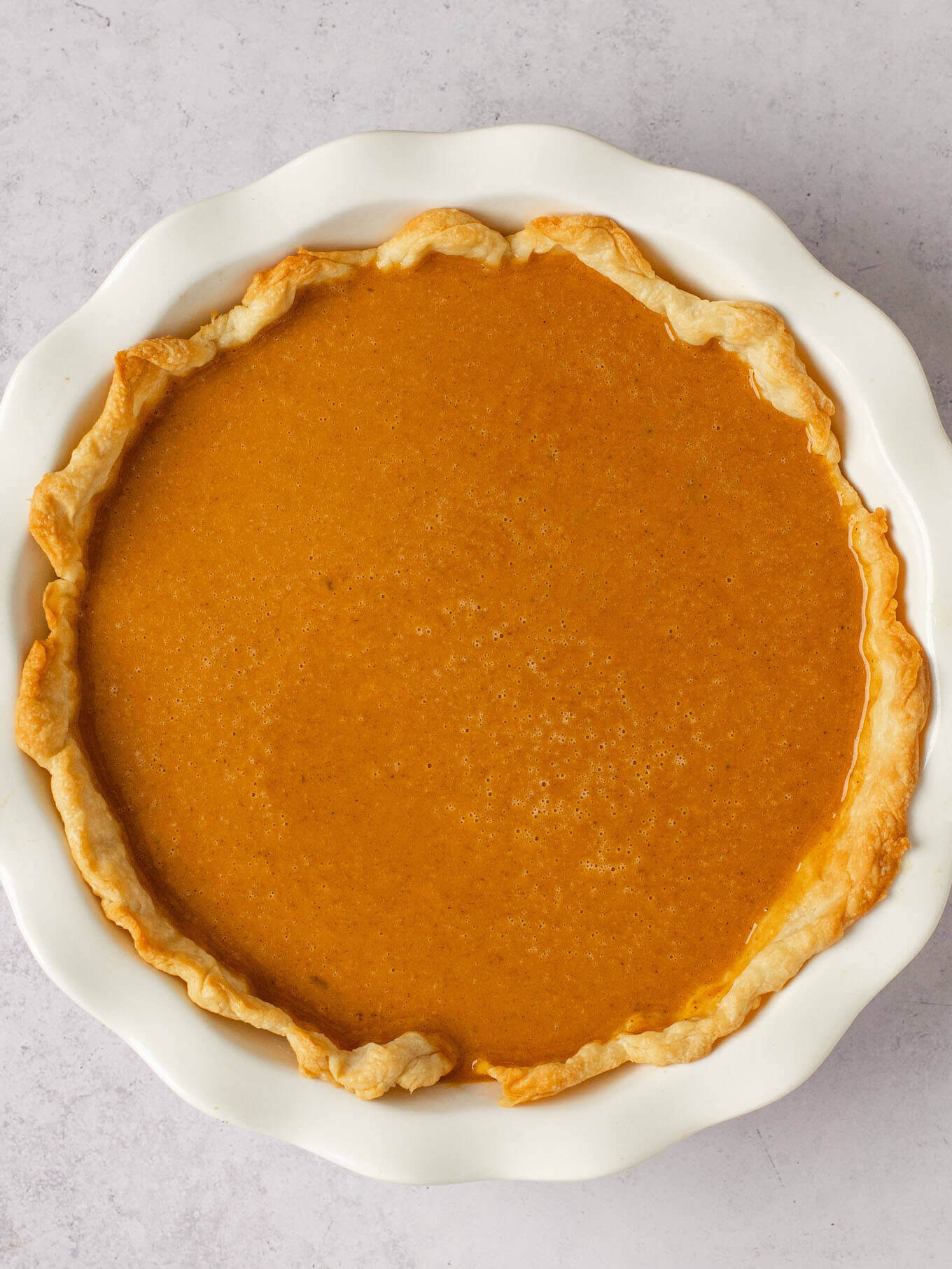 An overhead view of a partially baked pie crust filled with the pumpkin pie filling.