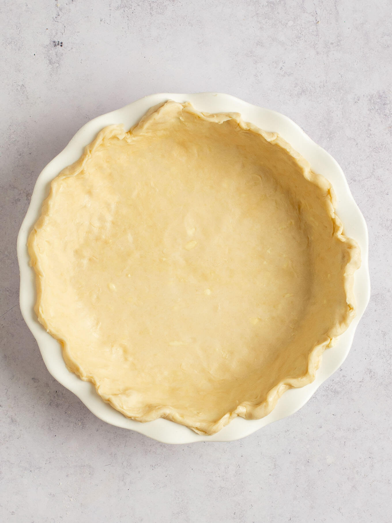 Pie dough in a white pie dish with the edges crimped.