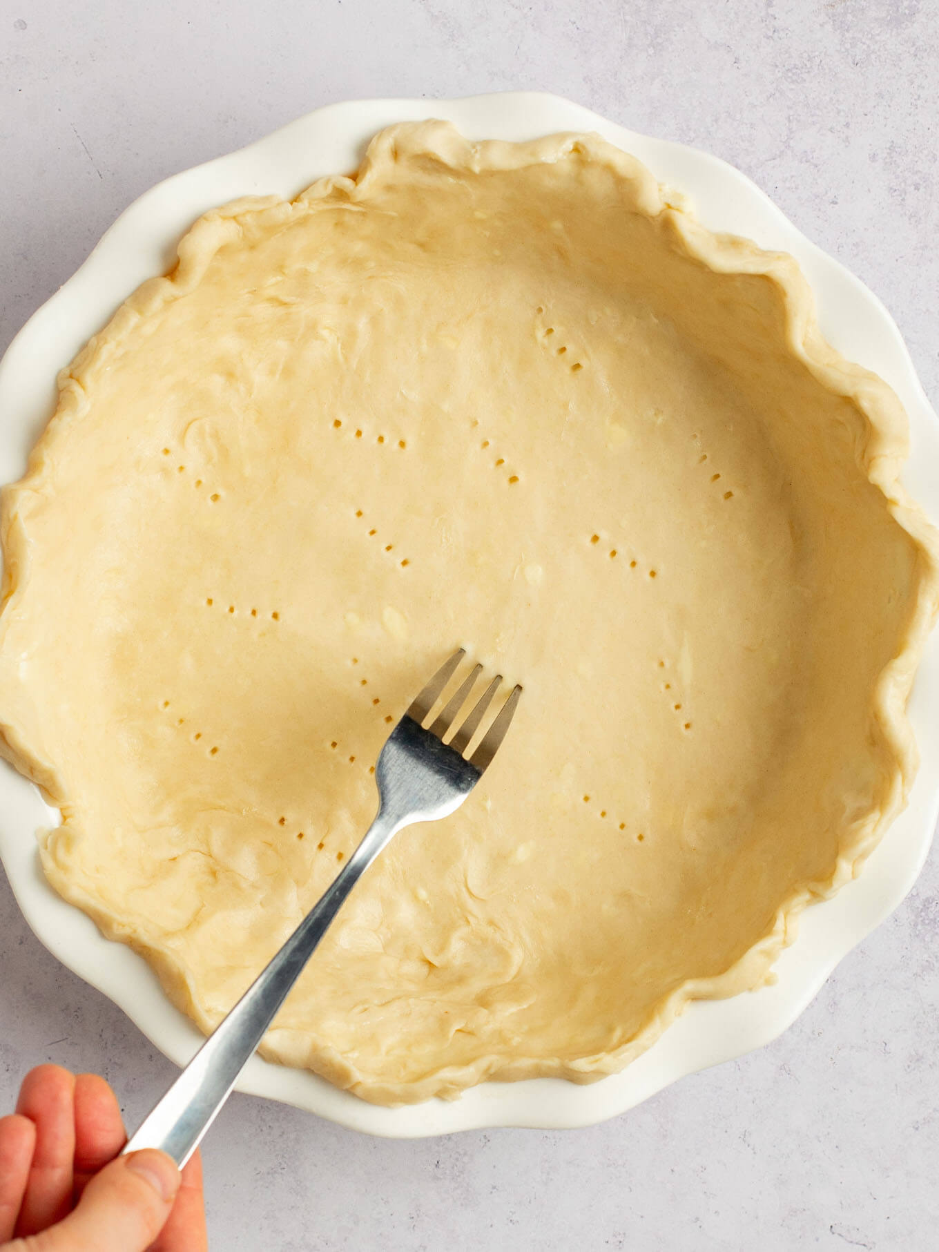 An overhead view of a fork being used to poke holes in the bottom of the raw pie crust.