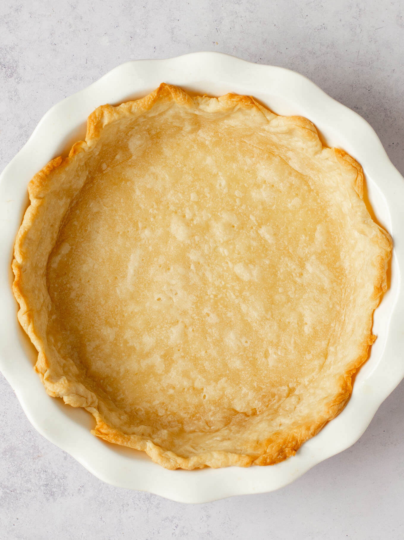 A partially baked pie crust in a white pie dish.